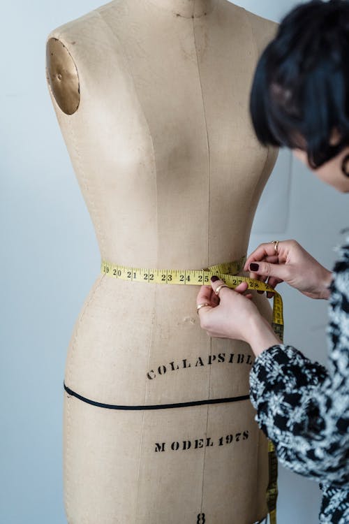 Female designer measuring waist of mannequin