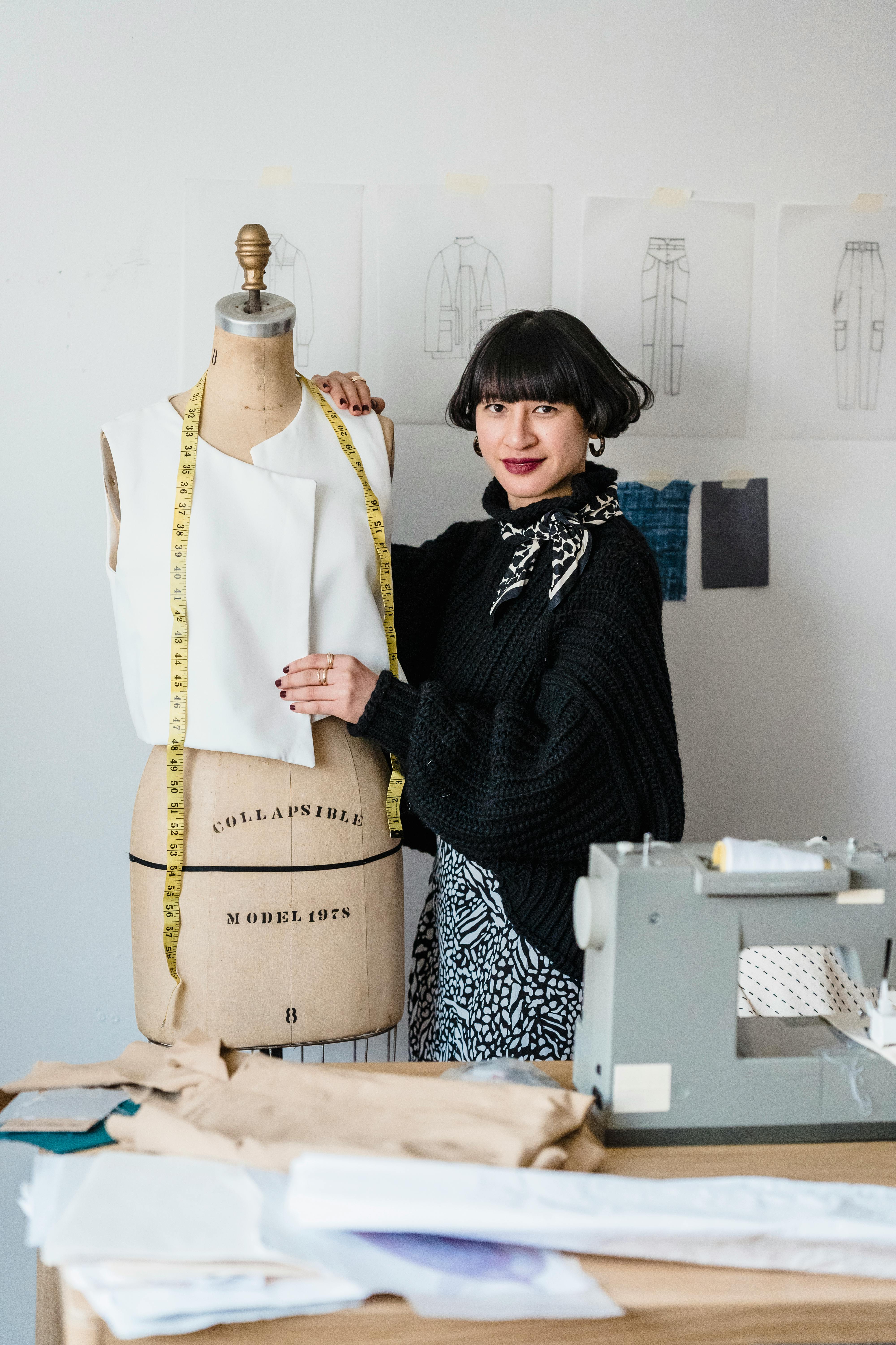 positive asian female sewing standing near mannequin during work in atelier