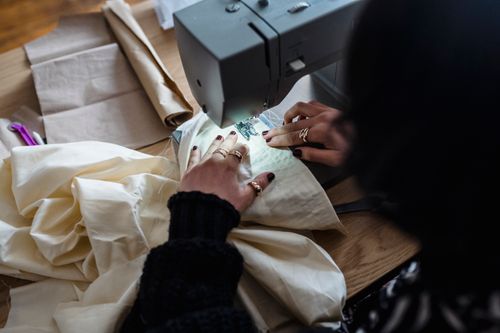 Free From above of crop unrecognizable female dressmaker sitting at wooden table and sewing on sewing machine Stock Photo