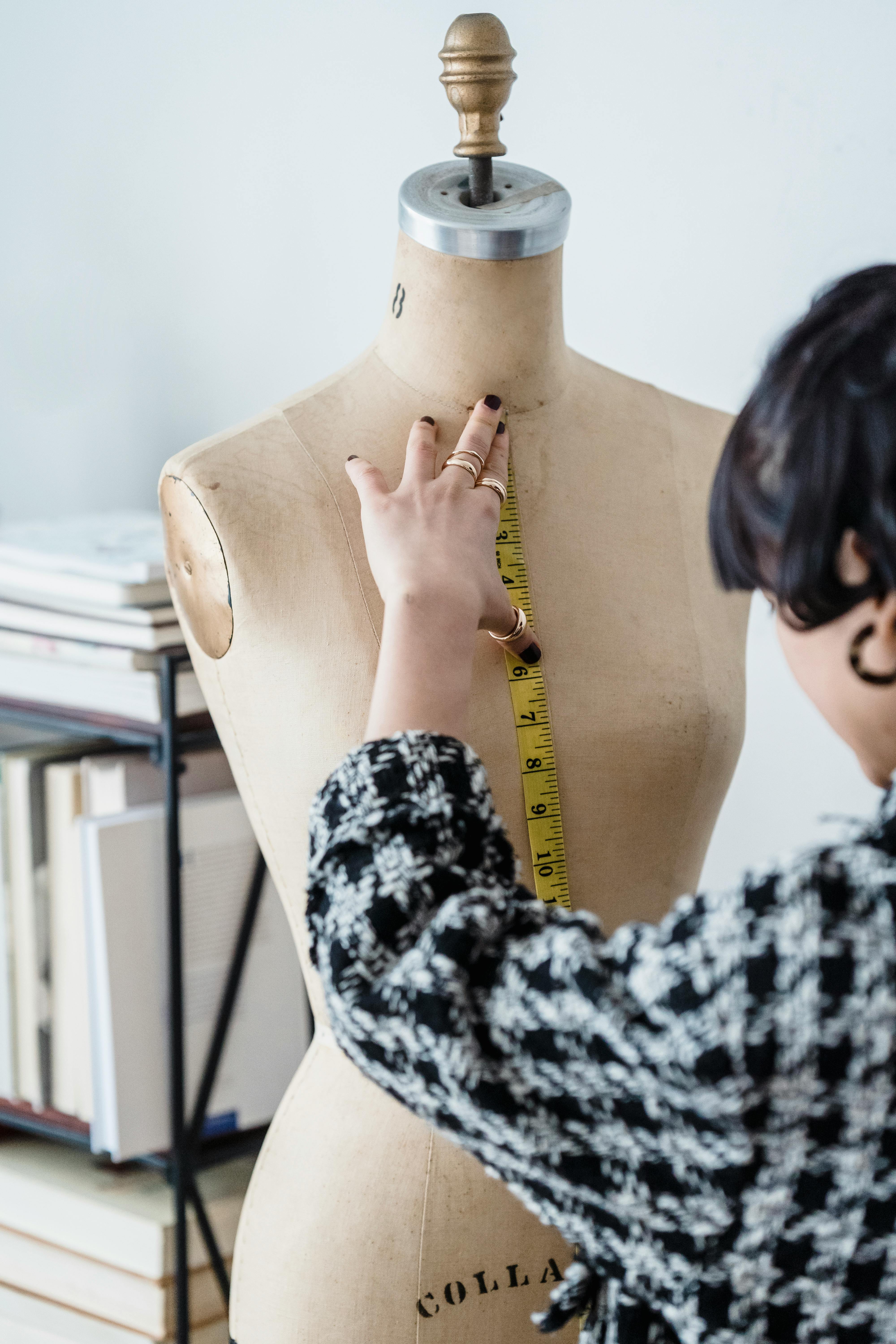 Mannequin Dress Form With Measuring Tape In Front Of Clothing Rack