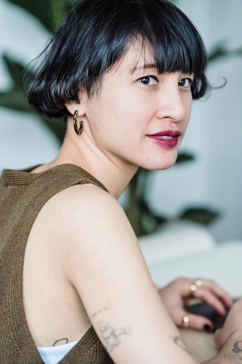 Calm Asian female with short dark hair and makeup sitting in light workspace on blurred background