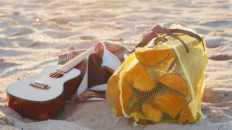 Guitar And Bag Of Firewood On Beach Sand