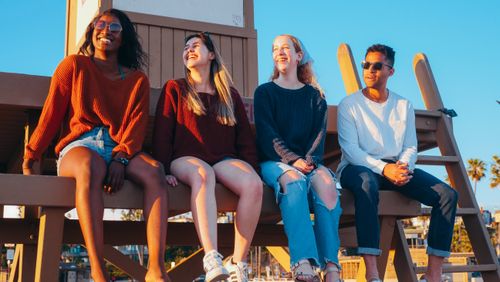Free A group of friends laughing and relaxing on a lifeguard tower at sunset by the beach. Stock Photo