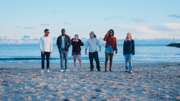 Diverse group of adults socializing on a sandy beach during sunset.