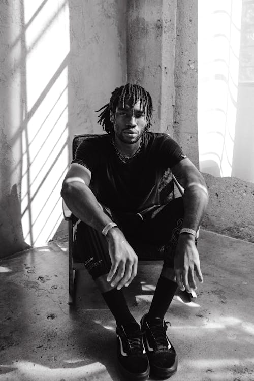 Grayscale Photo of a Man with Dreadlocks Sitting on a Chair