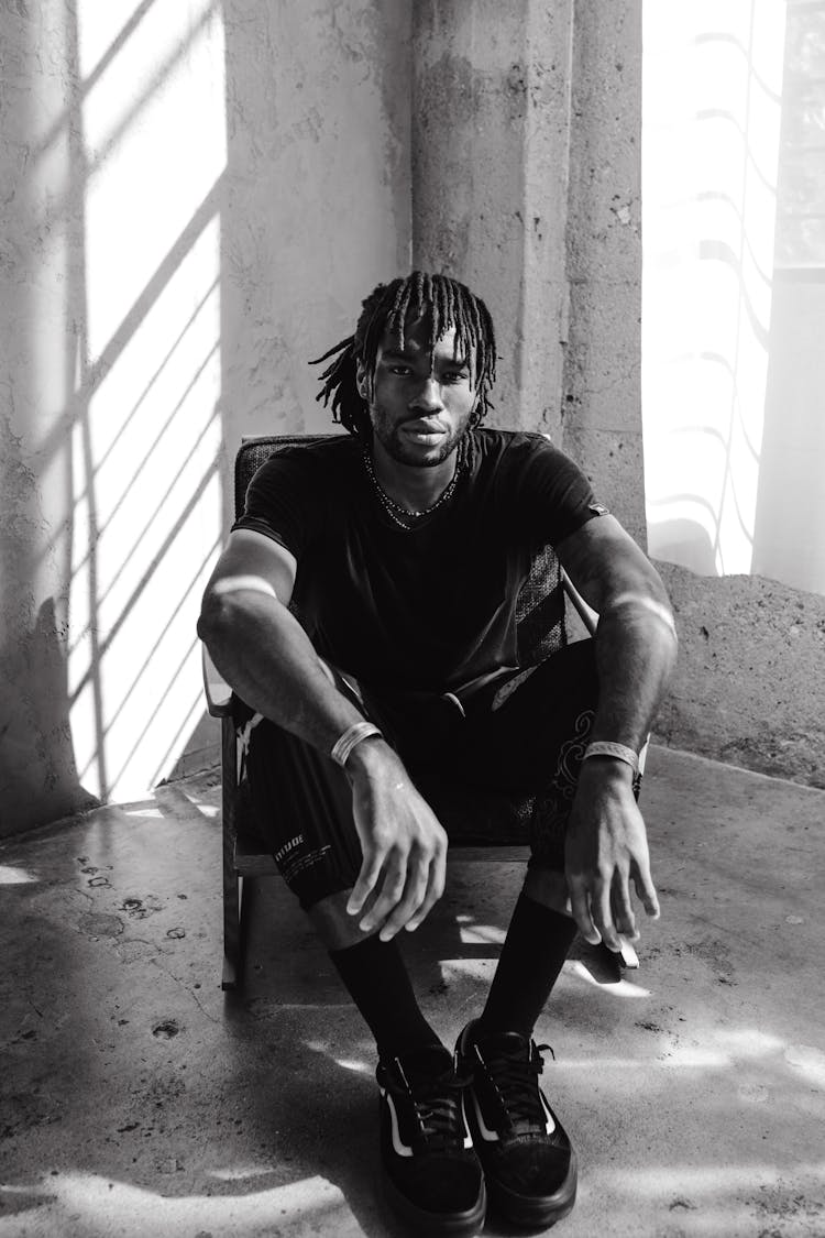 Grayscale Photo Of A Man With Dreadlocks Sitting On A Chair