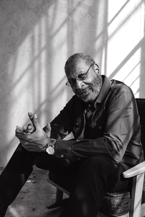 Grayscale Photo of a Man with Eyeglasses Sitting on a Chair