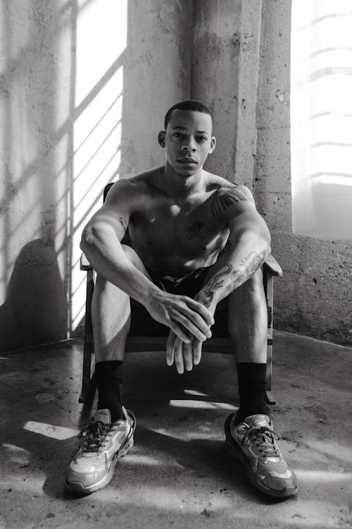 Grayscale Photo of a Shirtless Man Sitting on a Chair