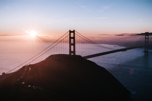 Breathtaking aerial view of the Golden Gate Bridge during sunrise, enveloped in morning fog.