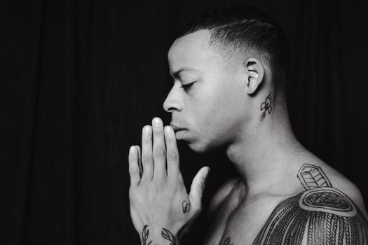 Side view of a tattooed man with closed eyes in contemplative prayer position.