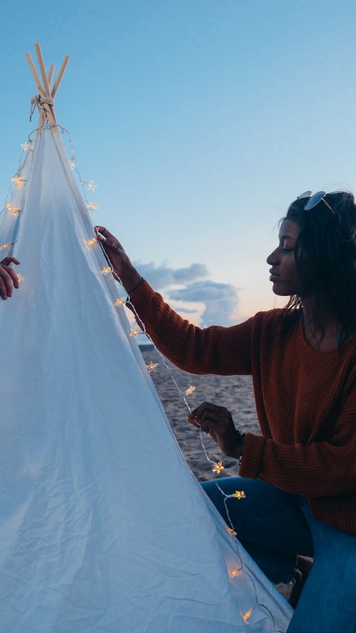 Free A woman decorates a teepee with string lights at sunset on the beach. Stock Photo