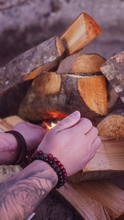 Free Tattooed and bracelet-adorned hands arranging firewood on a campfire. Stock Photo