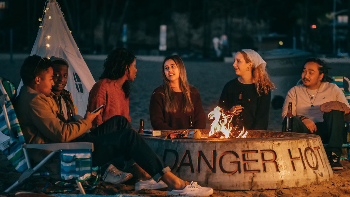 Three friends seated around a glowing bonfire at sunset, relaxed and connected in warm evening light