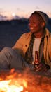 一名男子晚上在篝火旁喝啤酒，表现出放松和友谊