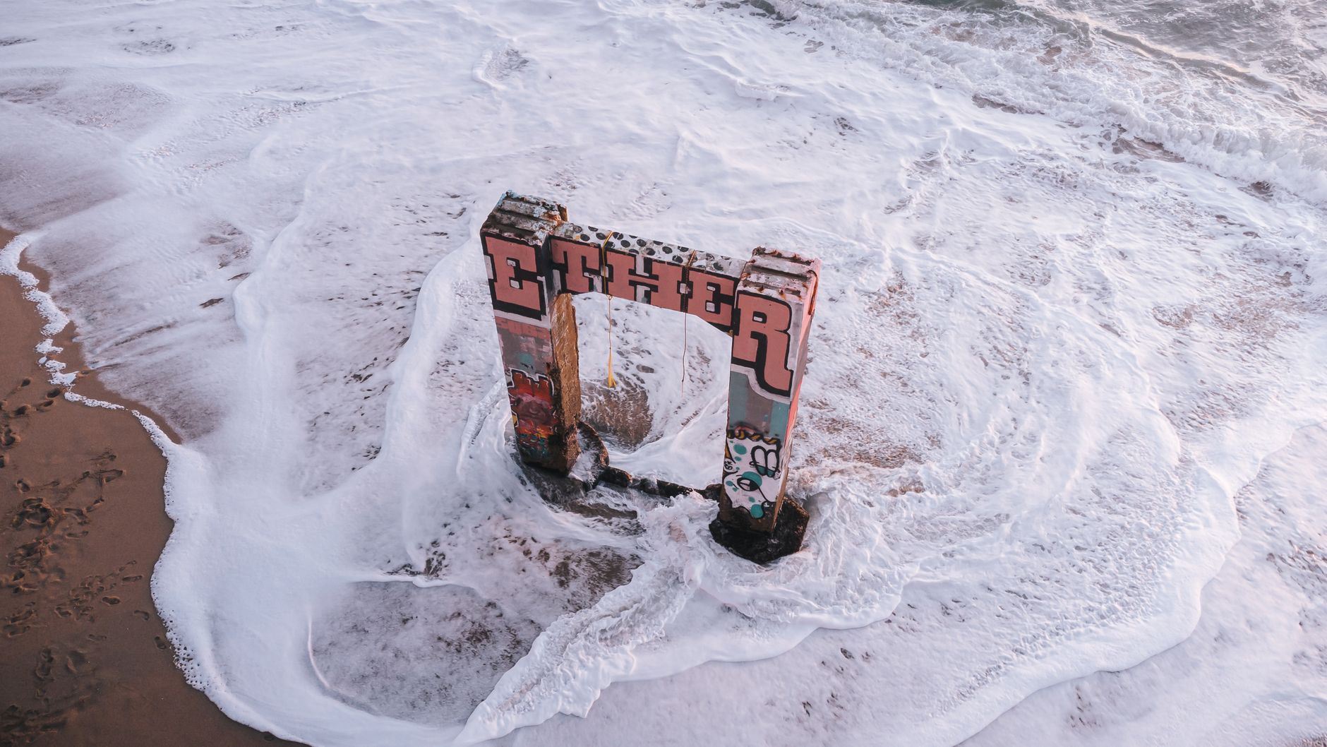 An aerial shot of graffiti-covered ruins amidst the sea foam at Davenport Beach, CA.