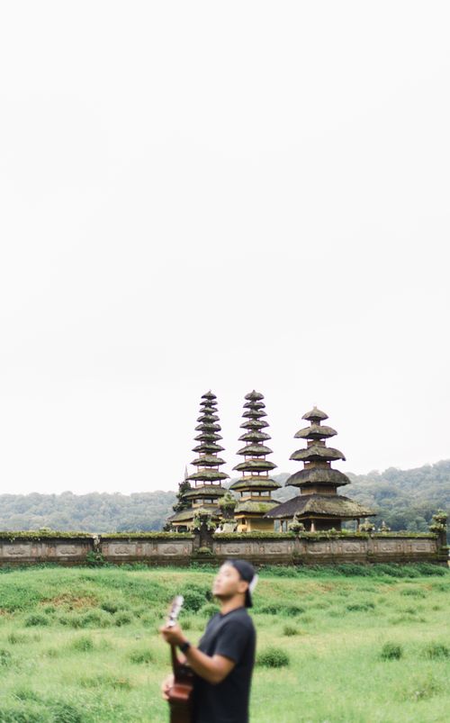 Free A man playing guitar in front of a traditional Balinese temple surrounded by lush greenery. Stock Photo