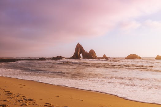 Dramatic rock formations at sunset on Martins Beach with gentle waves and pastel skies.