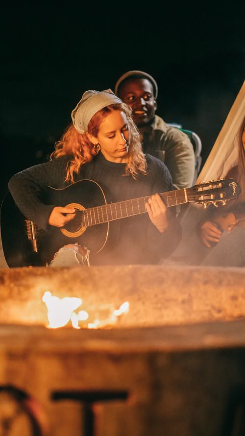 Free Friends enjoying a night campfire with acoustic music and camaraderie. Stock Photo