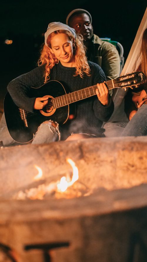 Free Group of friends playing guitar and singing by a campfire, creating a warm and joyful atmosphere at night. Stock Photo