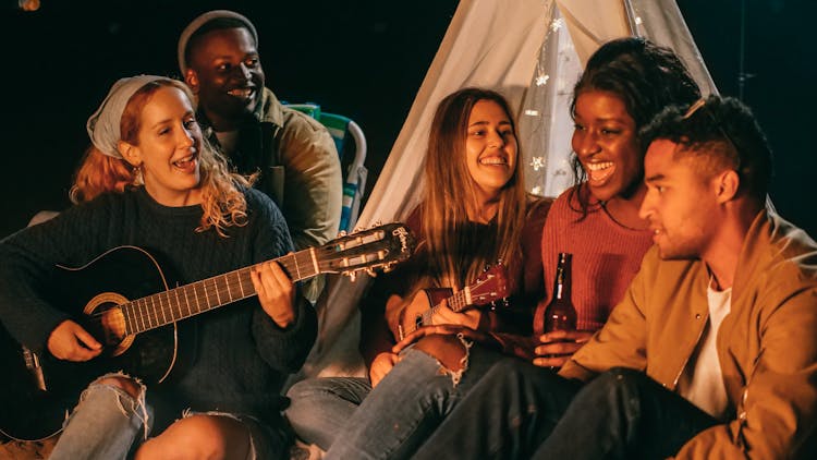 Group Of Friends Singing While Sitting On Beach Shore