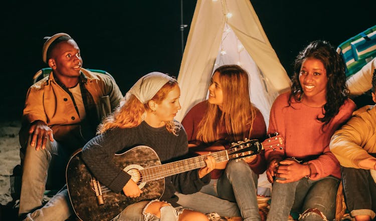 Group Of Friends Singing While Sitting On Beach Sand