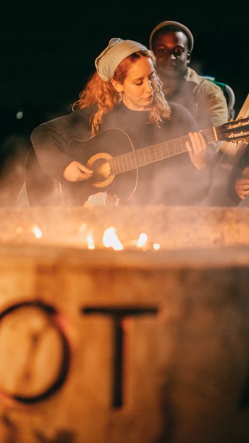 Free A group of diverse friends enjoying music by a campfire at night. Stock Photo