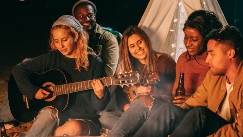 Free A group of friends enjoying music and drinks around a tent at night. Stock Photo