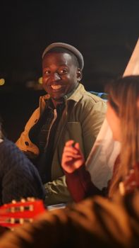 A lively night scene of friends enjoying music and laughter by a campfire.