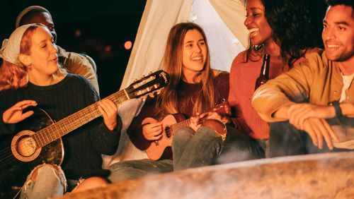 Free Group of friends relaxing and playing music around a campfire at night, enjoying a social outdoor gathering. Stock Photo