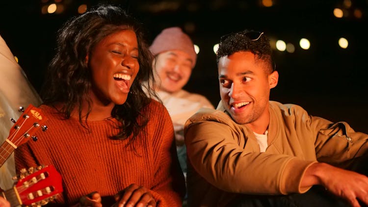 Group Of Friends Singing While Sitting On Beach Sand