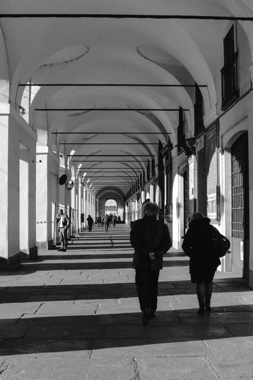 Free Black and white of unrecognizable people walking in hall of old stone building with arched ceiling and shades in sunlight Stock Photo