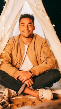A young man enjoying a relaxing night in a teepee illuminated by cozy string lights.