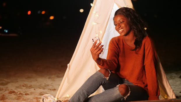 Woman enjoying a nighttime beach hangout, snapping selfies by a tent.