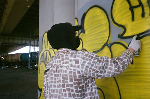 Man in Plaid Jacket Spray Painting a Wall