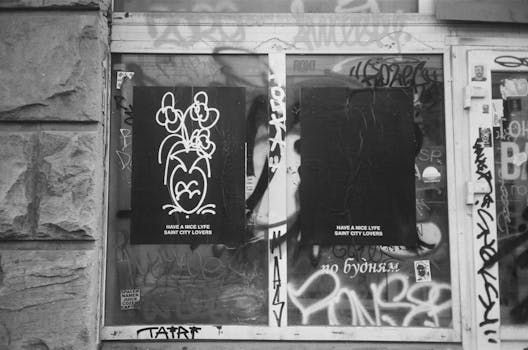 Monochrome photo of an abandoned city shop window covered in graffiti and posters.