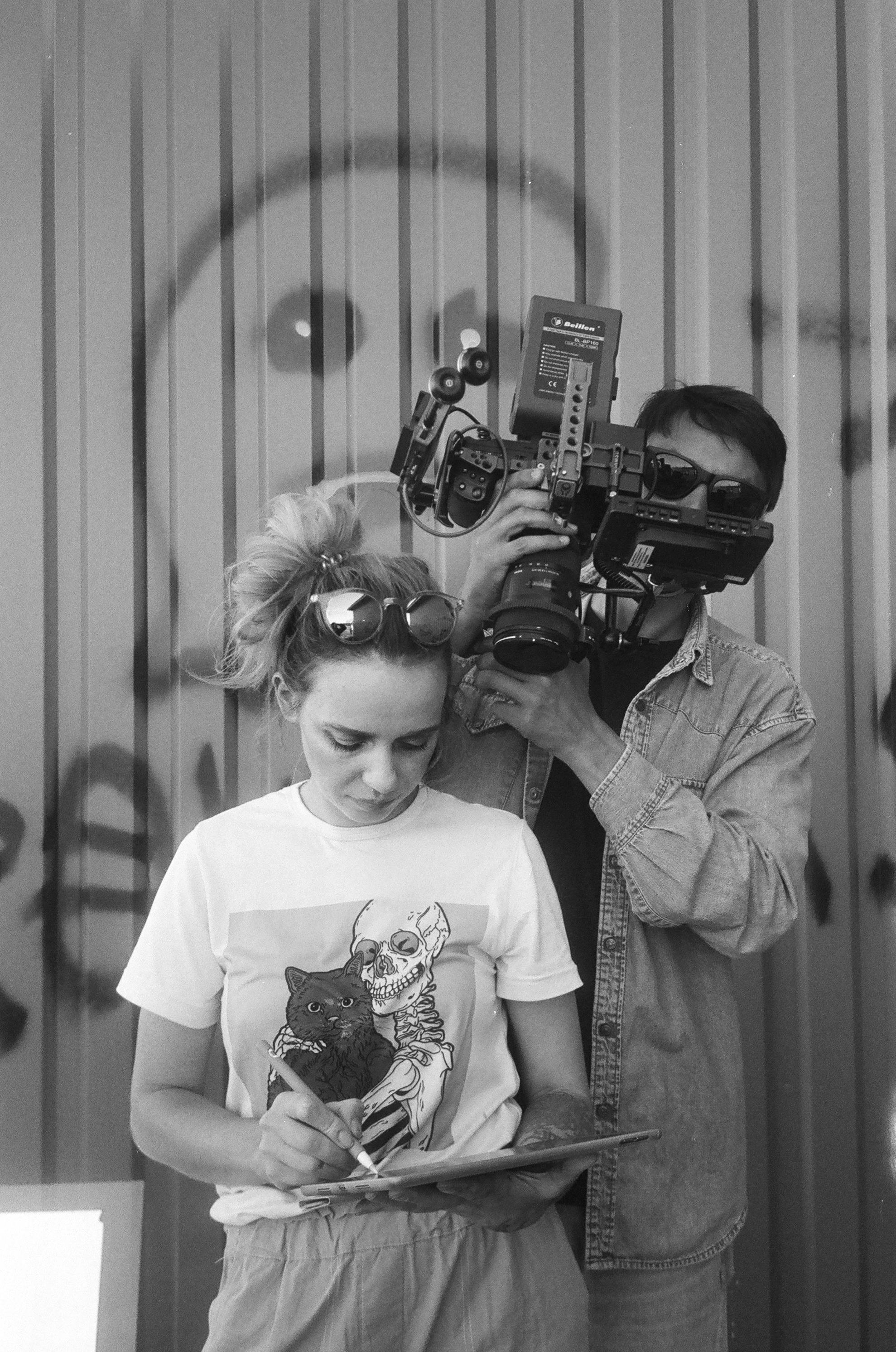 woman with pen standing in front of man holding camera