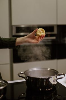 A hand holds fresh tagliatelle over a pot in a modern kitchen.