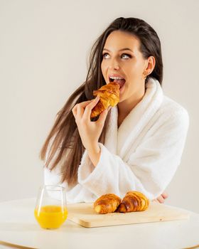 Woman in bathrobe enjoying croissants and orange juice for breakfast.