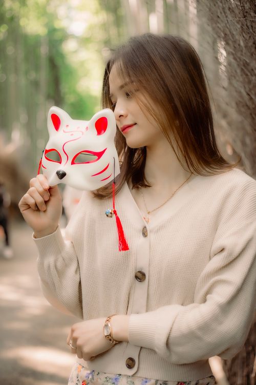 Free Portrait of an Asian woman holding a fox mask outdoors, capturing serene elegance. Stock Photo