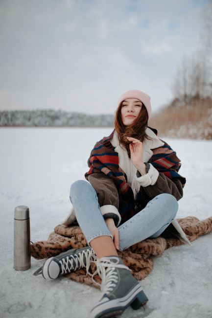 A young woman in winter attire sits on snow with ice skates and a thermos flask in Belarus.