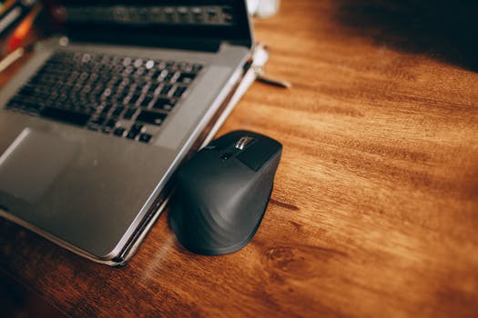 A wireless mouse and laptop placed on a polished wooden desk, perfect for office and remote work setup.