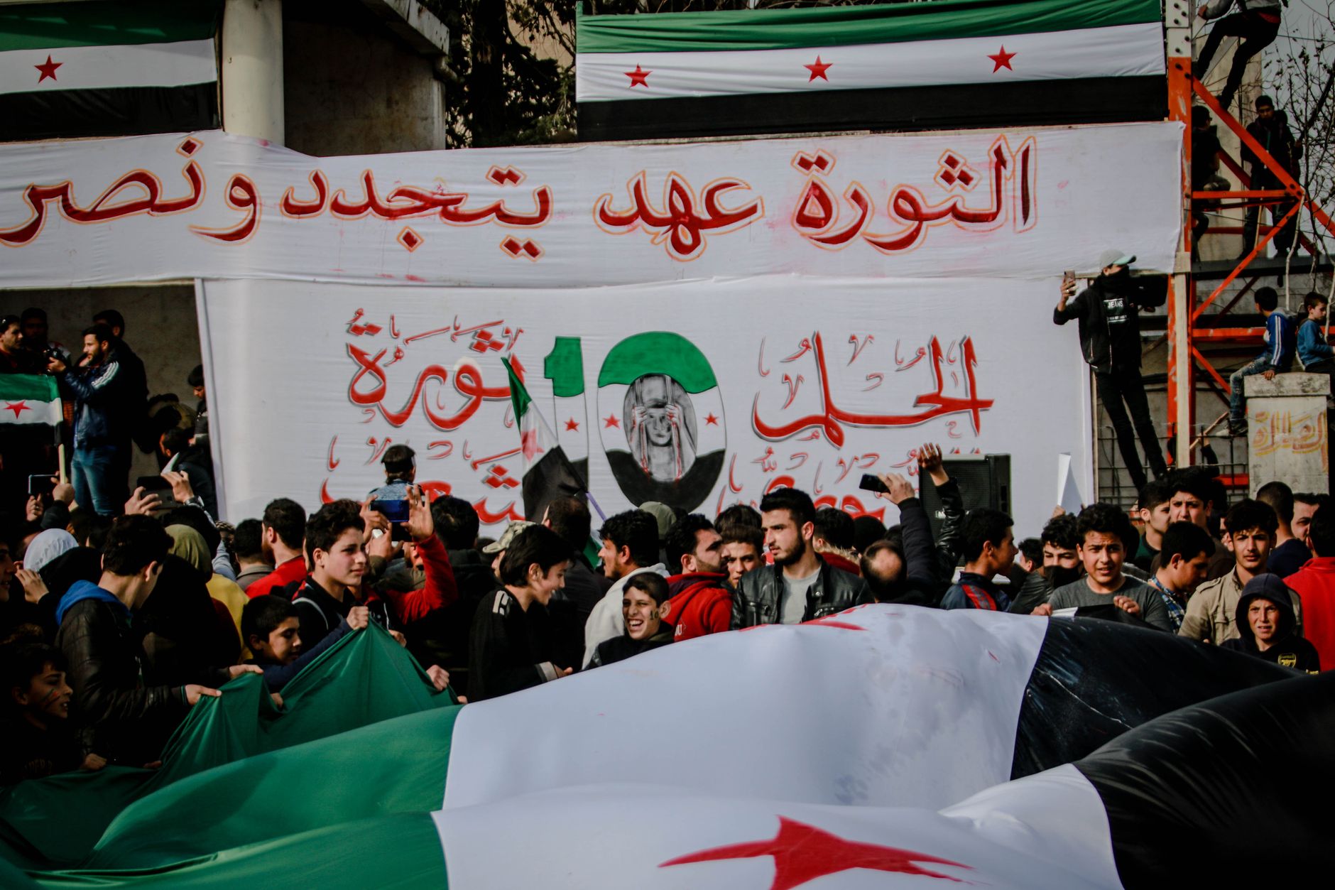 A large group protests in Idlib, Syria, demonstrating for political change with banners.
