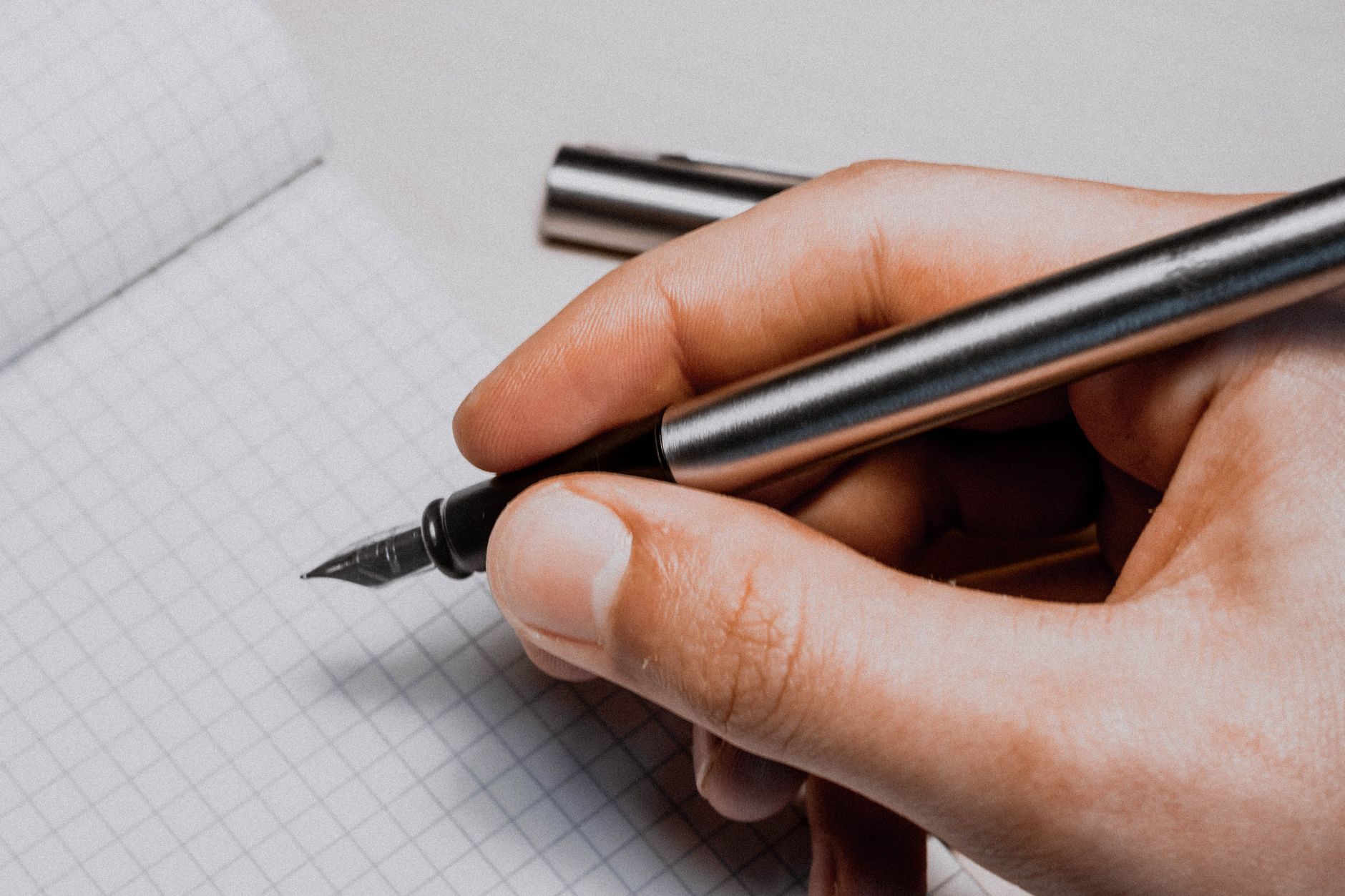 A hand holding a pen writing in a journal with a cup of coffee nearby