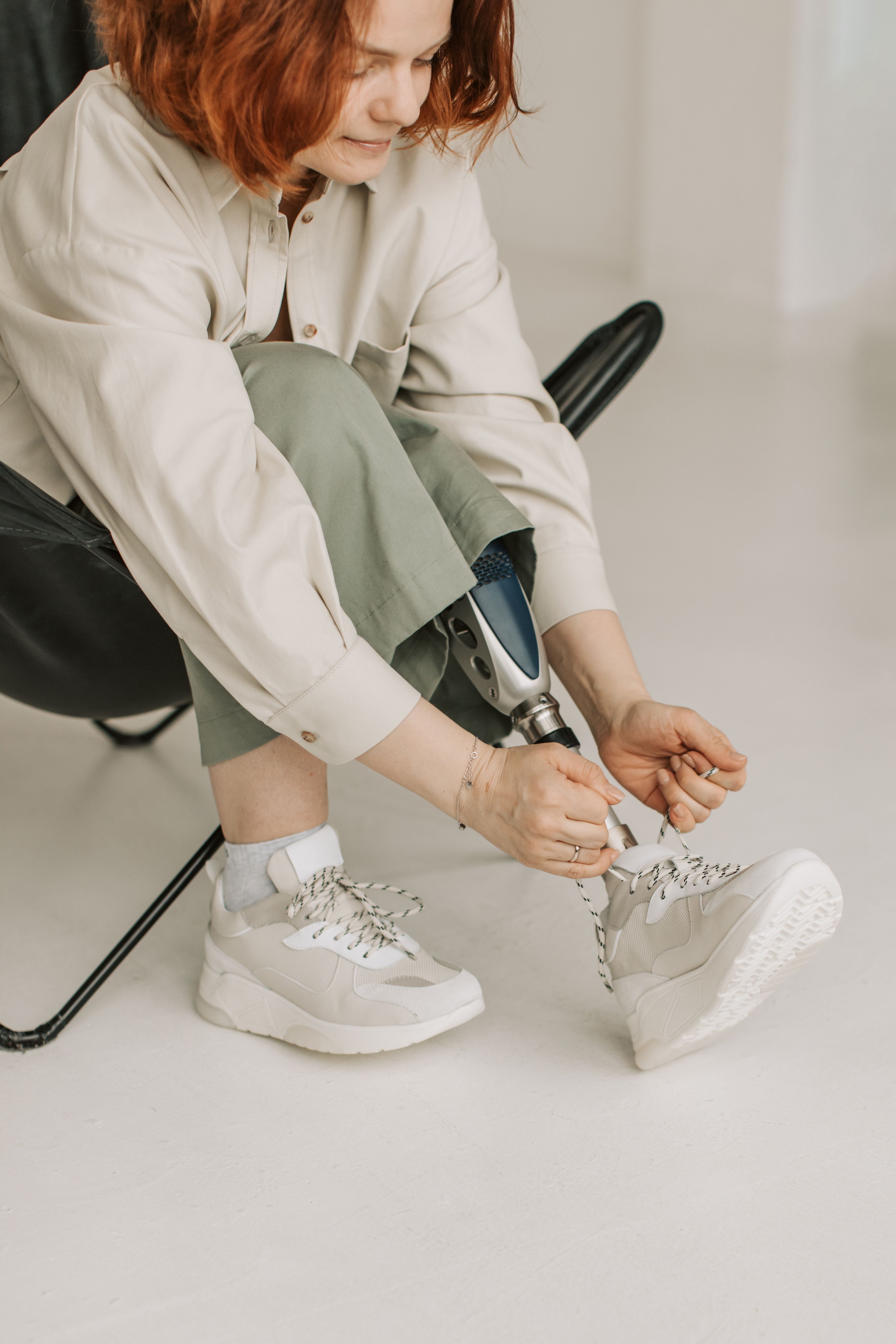 Caucasian woman with prosthetic leg tying her sneakers while sitting indoors, embracing modern lifestyle.