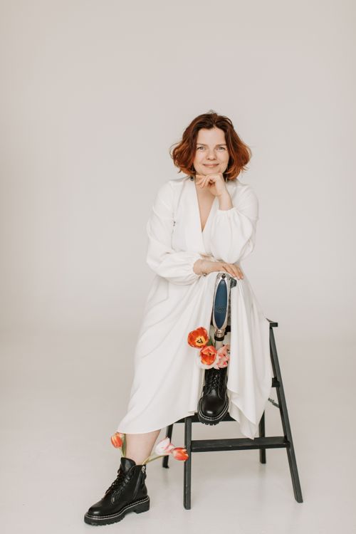 Free Woman with ginger hair posing in a white dress, showcasing a prosthetic leg adorned with flowers. Stock Photo