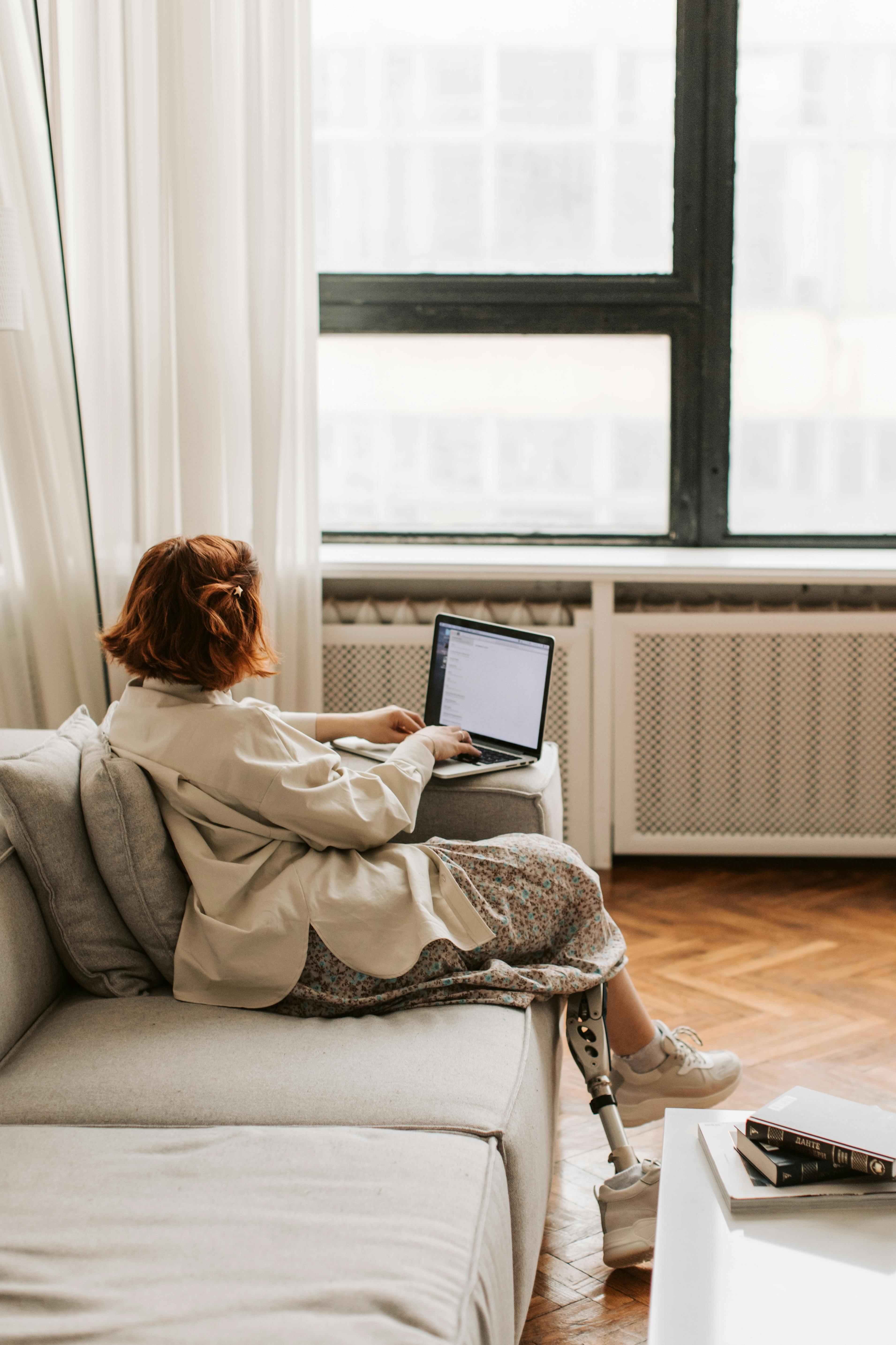 A woman with a prosthetic leg working on a laptop in a comfortable indoor setting, representing remote work and inclusivity.