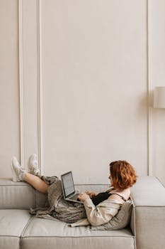 A woman relaxing and working from home on a cozy couch with laptop.