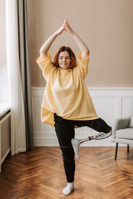 Woman practicing yoga indoors, showcasing balance and strength with a prosthetic leg.