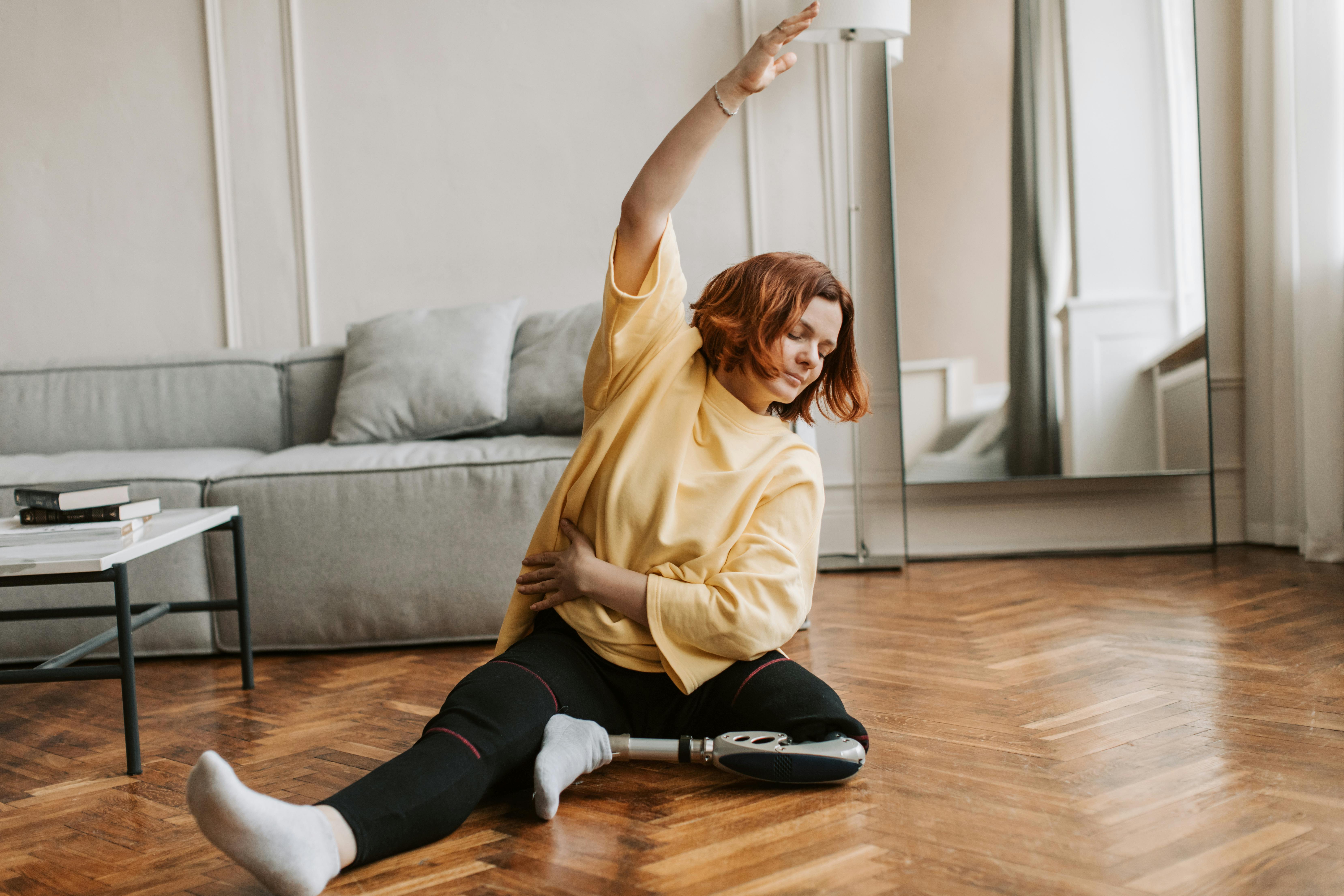 Caucasian woman with a prosthetic leg engaging in a stretching routine at home, emphasizing fitness and adaptability.