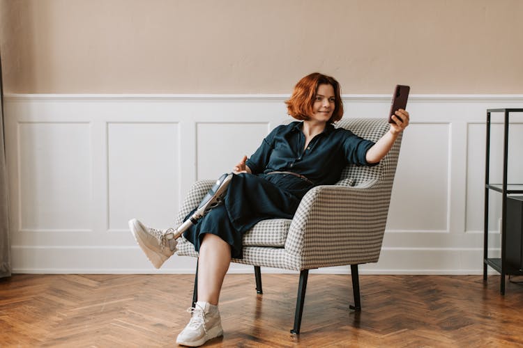 A Woman With Prosthetic Leg Sitting On The Chair While Using A Phone